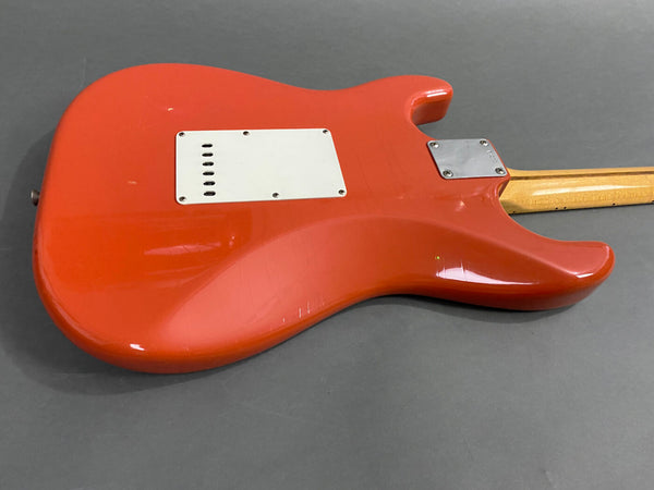 Rear view of red electric guitar body showing white tremolo cavity cover and wooden neck on gray background