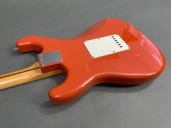 Back view of red electric guitar body with white plastic cover plate and maple neck on gray surface