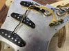 Close-up of vintage single-coil pickups and wiring on metal pickguard of electric guitar body showing electronic components and potentiometers.