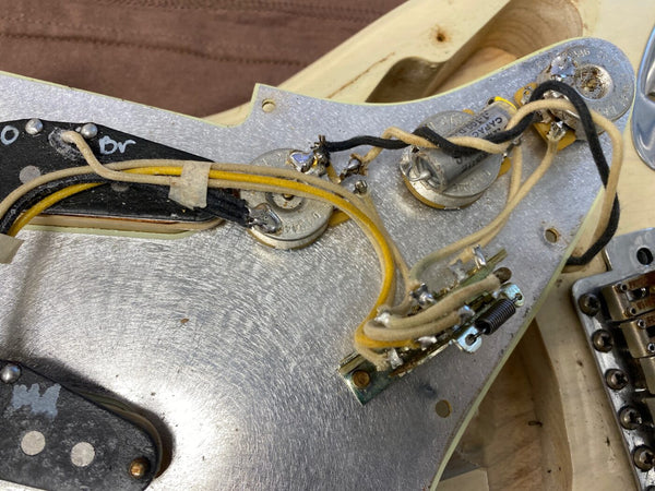 Close-up view of vintage guitar pickguard wiring with capacitors, potentiometers, and cloth-covered wires on an unfinished guitar body at Coffee House Guitars.