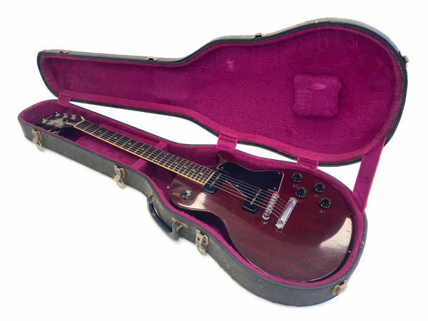 Vintage electric guitar with dark wood finish in black hard shell case lined with purple plush interior, featuring two pickups and multiple control knobs.