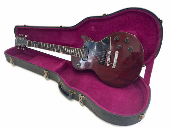 Vintage Gibson electric guitar with dark wood finish and black pickguard in open hard case lined with plush purple interior