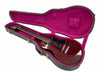 Electric guitar in dark red finish with black pickguard and control knobs, shown inside open hard guitar case with plush purple interior lining