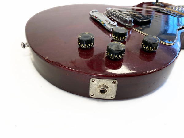 Close-up of vintage red electric guitar body showing four black control knobs, chrome bridge, pickup, and input jack plate on white background