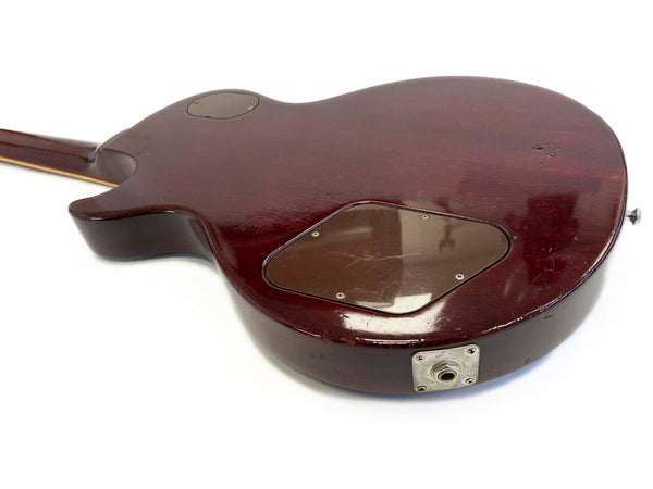 Back of vintage dark brown electric guitar body with control cavity cover plate and input jack visible, showing wear and scratches on wood finish