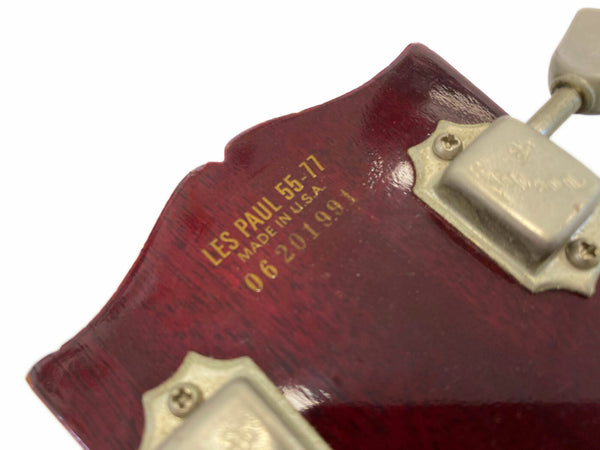 Close-up of Les Paul 55-77 guitar headstock showing serial number and Made in U.S.A. mark on dark red wood with gold lettering and vintage tuning pegs.