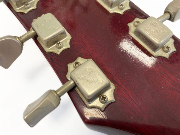 Close-up of vintage Gibson guitar tuning pegs on dark red wooden headstock showing aged metal hardware and screws