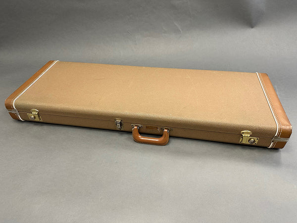 Brown vintage rectangular hard guitar case with leather handle and metal clasps on gray background