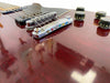 Close-up of vintage dark red electric guitar body showing chrome bridge, metal tailpiece, black pickup, and black volume and tone knobs with white numbering