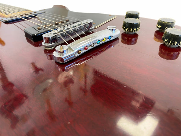 Close-up of vintage dark red electric guitar body showing chrome bridge, metal tailpiece, black pickup, and black volume and tone knobs with white numbering