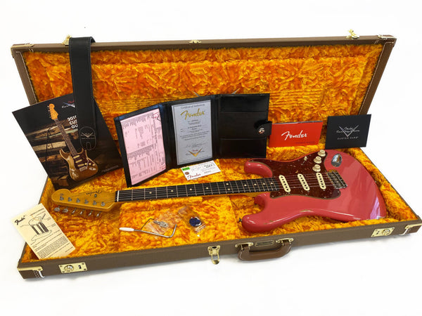 Fender electric guitar in candy apple red finish inside vintage-style hard case with yellow plush interior, including Fender owner's manual, certificate of authenticity, warranty card, tremolo arm, guitar strap, and assorted accessories.