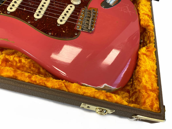 Close-up of worn red electric guitar body with white pickups and tortoiseshell pickguard in orange plush-lined guitar case