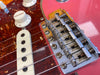 Close-up of red electric guitar bridge, Fender stamped saddles, white volume knob, and tortoiseshell pickguard with single-coil pickup and steel strings