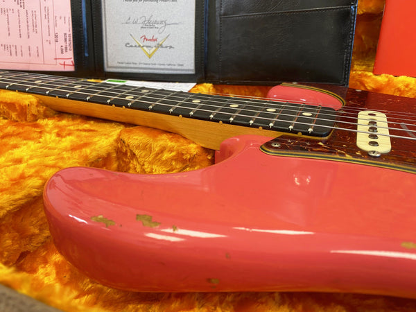 Close-up of vintage pink Fender electric guitar body and fretboard in a plush yellow hard case with certification papers visible in the background