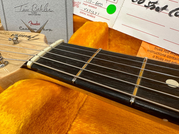 Close-up image of Fender Custom Shop electric guitar headstock and fretboard resting in a bright orange plush guitar case with certificate and documentation in background