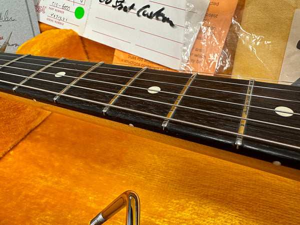 Close-up of vintage electric guitar rosewood fretboard with dot inlays and metal strings inside orange plush guitar case with paperwork