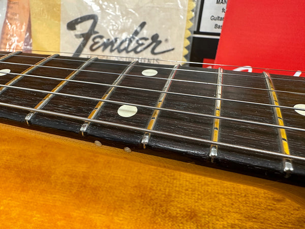 Close-up of Fender guitar fretboard with metal frets, dot inlays, and strings on a honey-colored wooden body