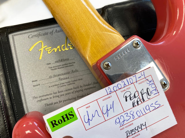 Close-up of Fender Custom Shop 61 Stratocaster Relic guitar neck plate with serial number R95444, certificate of authenticity, and RoHS compliance card on pink guitar body
