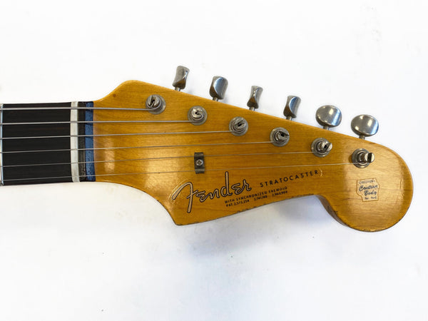 Close-up of vintage Fender Stratocaster electric guitar headstock with six tuning pegs and original contour body decal on light wood finish.