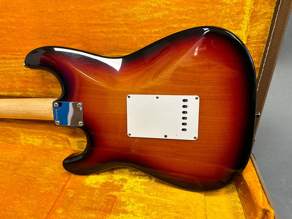 Electric guitar back body in sunburst finish with white plastic cover plate, displayed in an orange velvet-lined guitar case