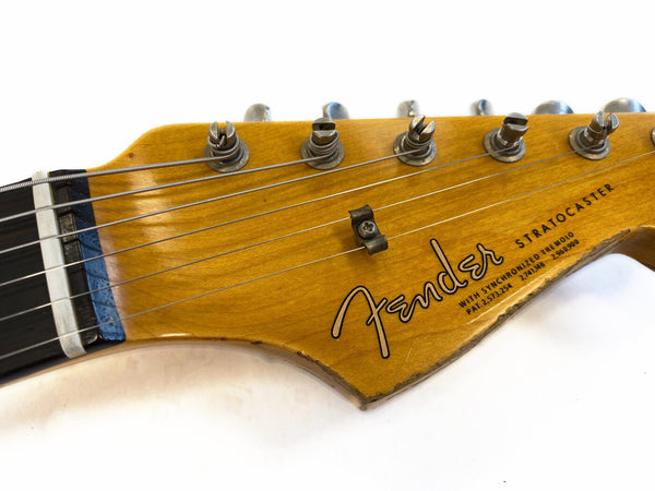 Close-up of vintage Fender Stratocaster guitar headstock with tuning pegs and strings, natural wood finish, showcasing Fender logo and serial numbers on white background.