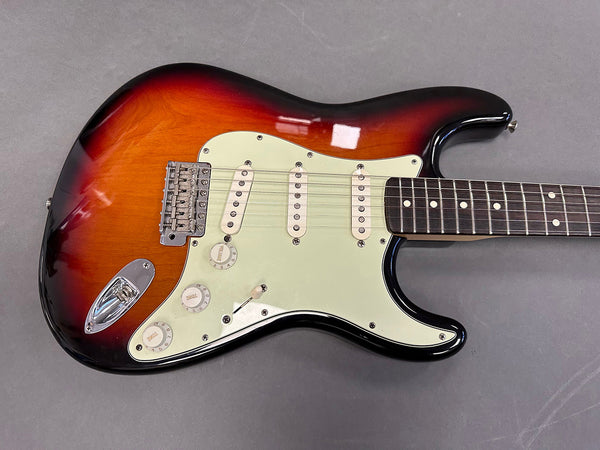 Sunburst electric guitar body with white pickguard and three single-coil pickups on gray background