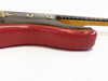 Close-up of worn red electric guitar body with tortoiseshell pickguard and maple neck on white background