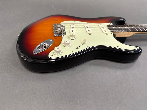 Sunburst electric guitar with white pickguard and three single-coil pickups on grey surface