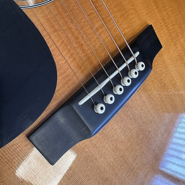 Close-up of acoustic guitar bridge with six white bridge pins and metal strings on natural wood body with black pickguard detail