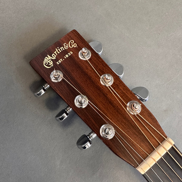 Close-up of Martin & Co. acoustic guitar headstock with tuning pegs and strings on gray background
