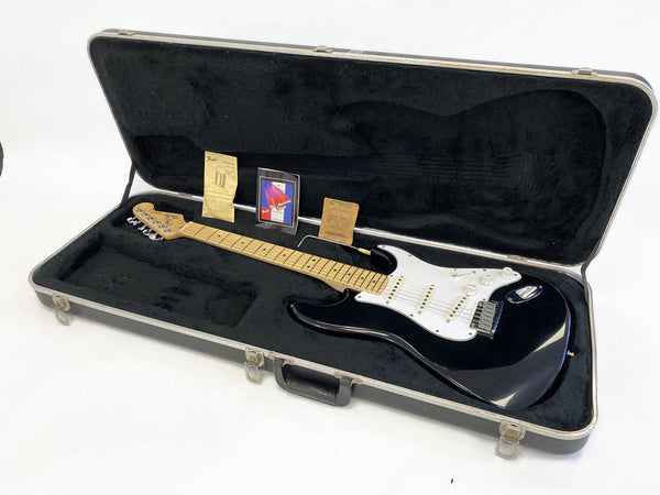 Black Fender Stratocaster electric guitar with maple neck and white pickguard in a black plush-lined hard case with manuals and accessories