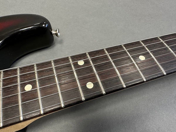 Close-up of black electric guitar neck and fingerboard with dot inlays and metal frets on gray background