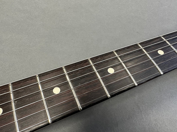Close-up of dark wood guitar fretboard with metal frets and dot inlays on grey background