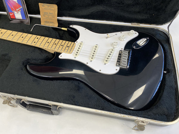 Fender American Series black electric guitar with maple neck in black plush-lined hard case with tremolo arm and control knobs visible