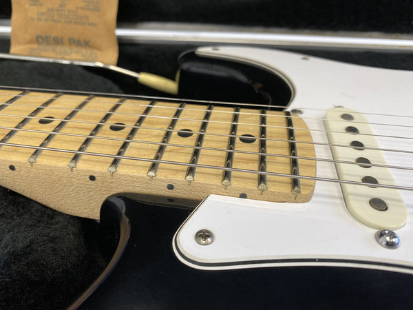 Close-up of electric guitar maple neck, frets, strings, and white single-coil pickup on black and white body with pickguard in guitar case