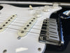 Close-up of electric guitar bridge, white single-coil pickups, and volume and tone control knobs on black and white guitar body