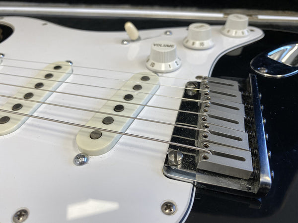 Close-up of electric guitar bridge, white single-coil pickups, and volume and tone control knobs on black and white guitar body
