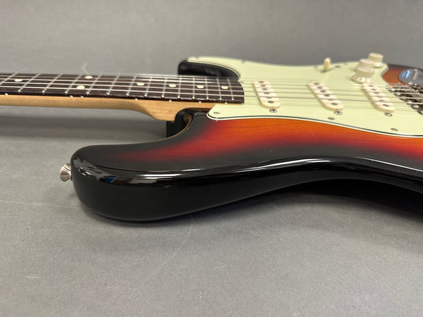 Close-up side view of sunburst electric guitar body with white pickguard and maple neck on gray background