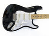 Black electric guitar with white pickguard and maple fretboard, three single-coil pickups, volume and tone control knobs, and chrome bridge on white background