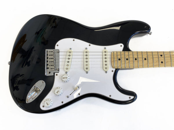 Black electric guitar with white pickguard and maple fretboard, three single-coil pickups, volume and tone control knobs, and chrome bridge on white background