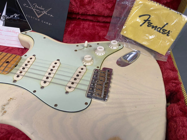 Close-up of vintage white Fender Stratocaster electric guitar body with three single-coil pickups, volume and tone knobs, and chrome bridge, shown in red plush guitar case with Fender yellow polishing cloth and Fender Custom Shop documentation.