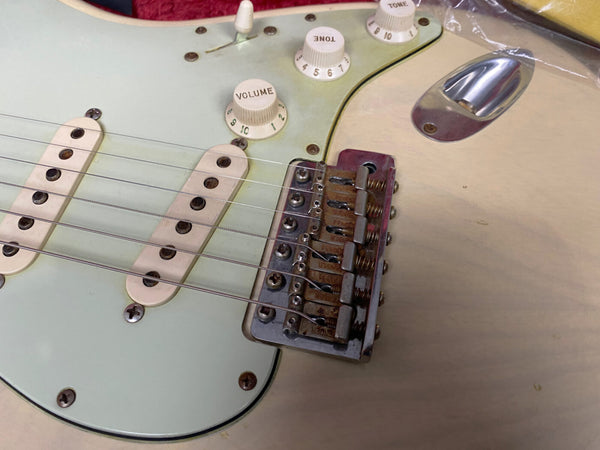 Close-up of vintage electric guitar bridge, pickups, and volume and tone control knobs on cream-colored body with aged pickguard