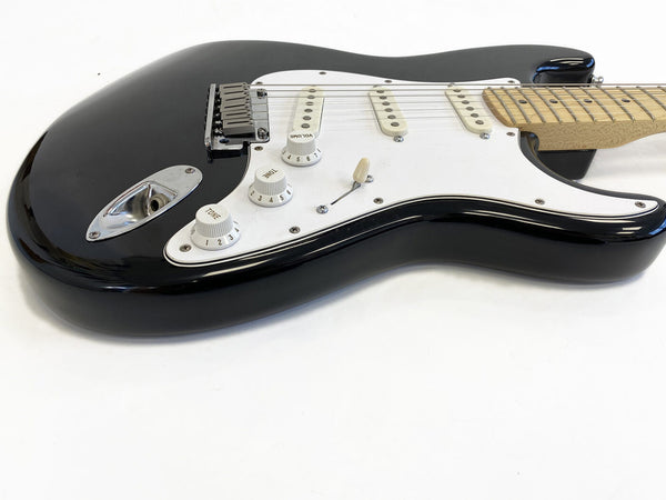 Black electric guitar with white pickguard and maple neck, three single-coil pickups, volume and tone control knobs, photographed on white background