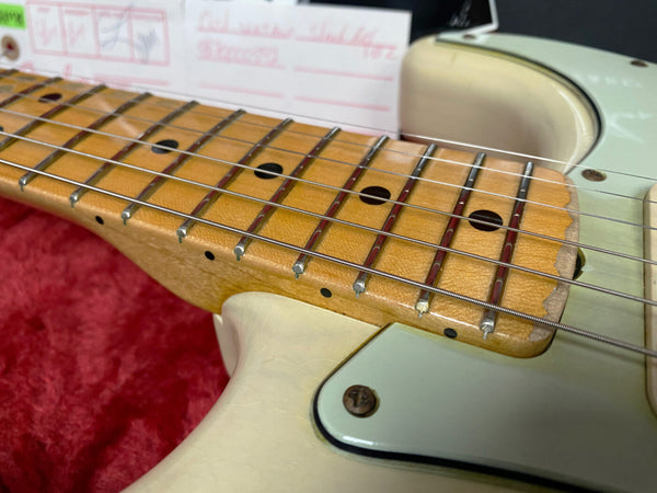 Close-up of vintage electric guitar neck and fretboard with worn maple wood and metal frets on white body with pickguard and strings, on red fabric background