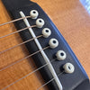 Close-up of acoustic guitar bridge with six white bridge pins and steel strings on natural wood top at Coffee House Guitars