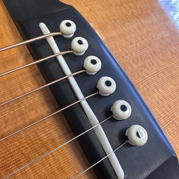 Close-up of acoustic guitar bridge with six white bridge pins and steel strings on natural wood top at Coffee House Guitars