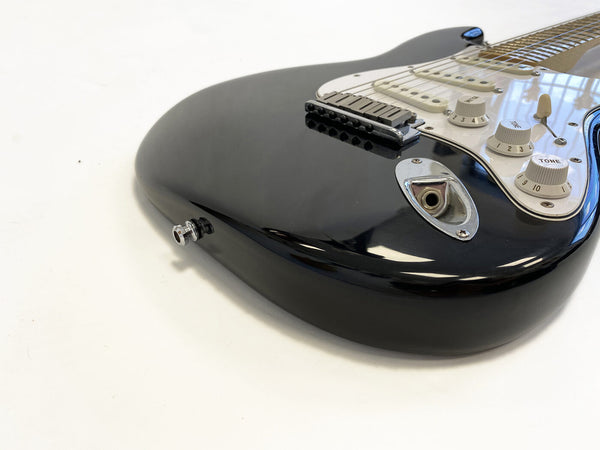 Close-up of black electric guitar body with white pickguard, tone and volume knobs, and input jack on white background