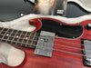 Close-up of vintage red electric bass guitar body with metal pickups and black pickguard inside plush guitar case with owner's manual