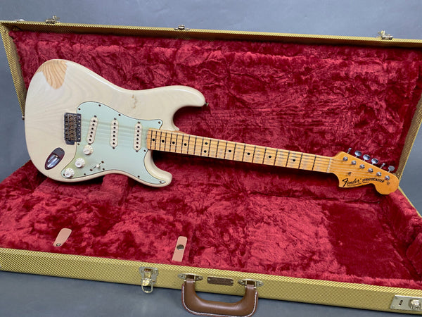 Vintage Fender Stratocaster electric guitar with maple neck and aged white body, displayed in open tweed hard case with red plush interior