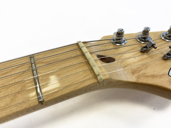 Close-up of natural wood guitar neck and headstock showing tuning pegs, nut, strings, and fret wire on electric guitar
